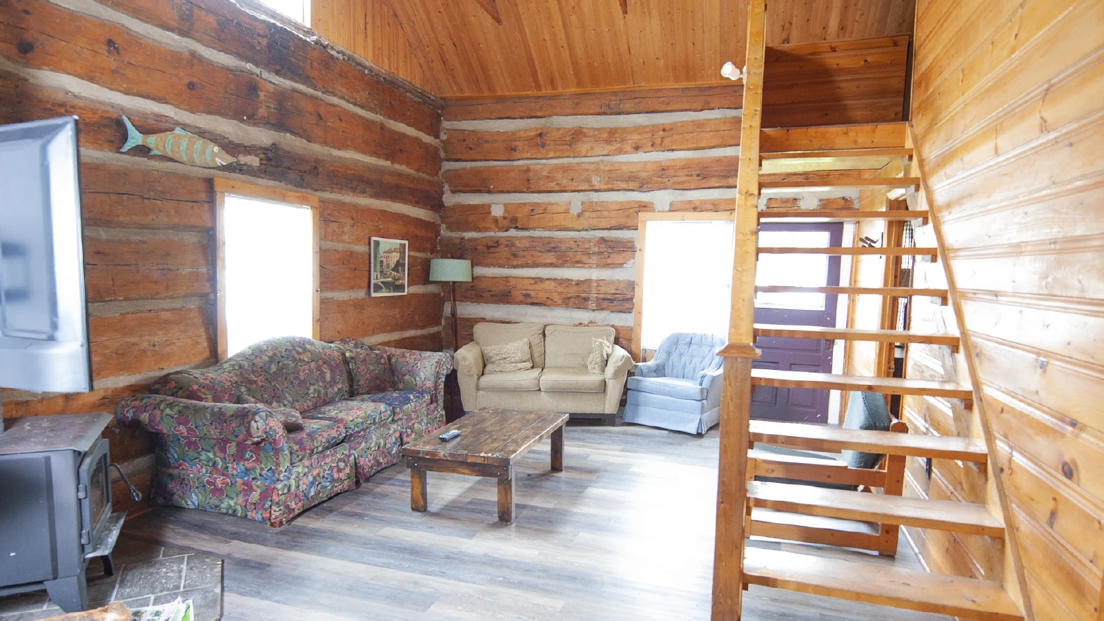 Pigeon Lake Resort Cottage Seven.&nbsp; Log cabin living room with sofas, wood stove, and staircase to loft.